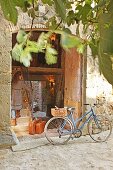 Bicycle with basket in front of open door of stone house; woman with leather suitcases waiting on stairs