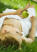 Young woman lying in grass, holding apple