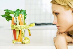 Young woman looking at glass full of vegetables with a measuring tape bow, profile