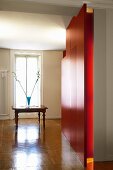 Glossy herringbone parquet in grand hallway with red wall and antique table in front of French window