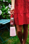 Frau trägt Flasche mit Nektarinen-Himbeer-Smoothie im Garten