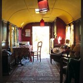 Cosy interior of converted railway carriage with Oriental rug and red lanterns hanging from yellow ceiling