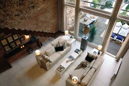 View from above of a sofa landscape in a spacious living room with a bank of windows and natural stone and brick wall