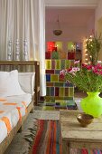 Sofa with white cushions next to rustic coffee table and half-height partition of coloured glass bricks next to white curtain