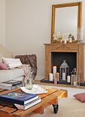 Table made of pallet on castors and pale sofa in front of lit candles in fireplace below wall mirror on mantelpiece