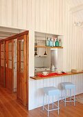 Breakfast counter and bar stools at hatch in open-plan attic apartment with wood-clad walls