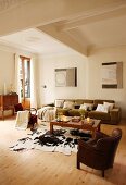 Leather armchair in front of cow skin rug on wooden floor and modern sofa in seating area of simple living room with traditional ambiance