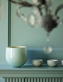 Elegant china bowl and tiny dishes on mantelpiece in front of profiled wooden wall panel