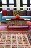 Colourful rug in front of onion-shaped vase on vintage coffee table and blue sofa with patterned cushions