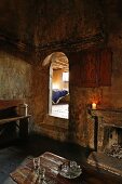 Kaminzimmer in altem Haus mit verrussten Wänden und Blick durch offenen Durchgang mit Rundbogen auf ein Bett