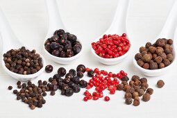 Allspice berries, pink pepper, juniper berries and black peppercorns on spoons