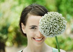 Frau hält blühenden Allium vor ihrem Auge