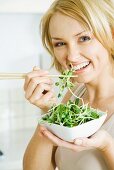 Woman eating radish sprouts with chopsticks, smiling at camera