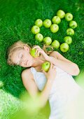 Junge Frau liegt auf der Wiese neben einem Herz aus grünen Äpfeln