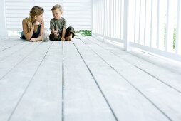 Mother and son on porch together, smiling at each other, boy holding butterfly, low angle view