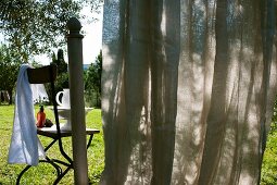 Curtain partially blocking view of chair with bathing utensils in garden