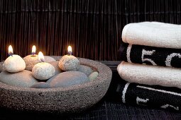 Relaxation in spa - lit pebble candles in stone dish next to stacked towels
