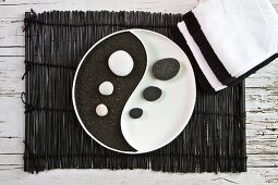 Yin and Yang dish with black pumice and white pebbles on bamboo mat