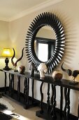 African antlers and busts of women on shelf below sunburst mirror