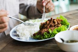 Person isst frittiertes Schweinefleisch mit Reis (Thailand)