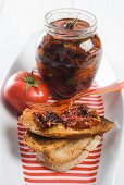 Eingelegte getrocknete Tomaten im Glas und auf Röstbrot