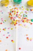 A white cake pop decorated with colourful sugar sprinkles