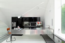 Wall lamp on swivelling arm above stainless steel kitchen counter and retro barstool in minimalist kitchen with black fitted cupboards