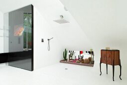 Exclusive bathroom with floor-level shower in front of collection of cacti in window niche, antique cabinet on white tiled floor and black sliding wall element