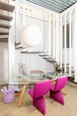 Simple glass table and chairs with pink upholstery below spherical pendant lamp in front of of winding staircase