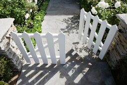 Gartenweg mit weiss lackiertem Gartentor, teilweise offenstehend