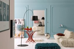 Arc lamp with black lampshade in front of glass table and sofa with white upholstery in living room with walls painted light blue