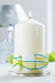 White pillar candle decorated with pebbles and rubber bands