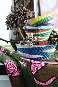 Hand-woven baskets of colourful wire in front of vase with floral relief elements on African fabric