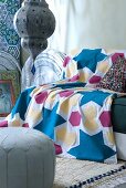 Gemusterte Tagesdecke auf Sofa und Ledersitzpolster vor tief hängender Deckenleuchte in orientalischem Stil