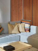 Cushions on light-coloured corner sofa in front of cupboard with door made of wooden slats