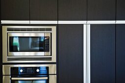 Microwave and oven surrounded by contemporary wooden cabinets