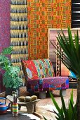 African style - colourful patterned chair in front of bright wall hangings surrounded by tropical potted plants