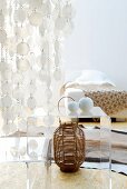 Dramatic, translucent capiz shell curtain above small, plexiglass table and basketwork vase; bed with simple bedspread in background