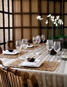 A table laid for an Asian meal, with bamboo wood place mats and white orchids in the centre of the table