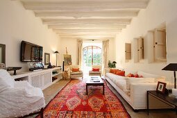 Wohnraum mit Orientteppich und weiss getünchter Holzbalkendecke in mediterraner Landhausvilla