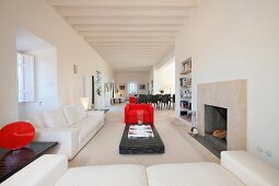 Moderner, mediterraner Wohnraum mit hellem Sofa und rotem Sessel vor offenem Kamin