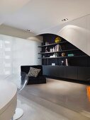 Modern living room - black low armchair in front of black and white built-in shelves on a platform