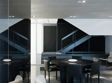 Round table made of dark wood with gray chairs in front of a staircase in a minimalist room