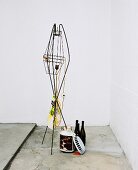 Partially disassembled fifties-style standard lamp and collection of bottles next to ornaments on concrete floor in corner of whitewashed room