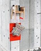Stool made from newspaper in front of red photo mount and child's stool made from reclaimed wood hanging on concrete wall