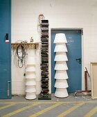 Stacked white lampshades in front of metal door next to modern bookcase