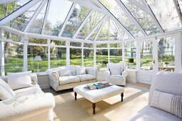 Spacious conservatory in extensive gardens; pale, traditional sofas and armchairs grouped around ottoman
