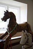 Large, antique rocking horse with artistic carved detail and smaller stuffed fabric horse in front of window