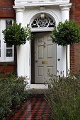Bay trees flanking stately entrance of English country house with brick facade and mosaic path edged by beds of lavender