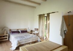 View from open-plan bathroom of double bed with shiny bedspread in simple bedroom